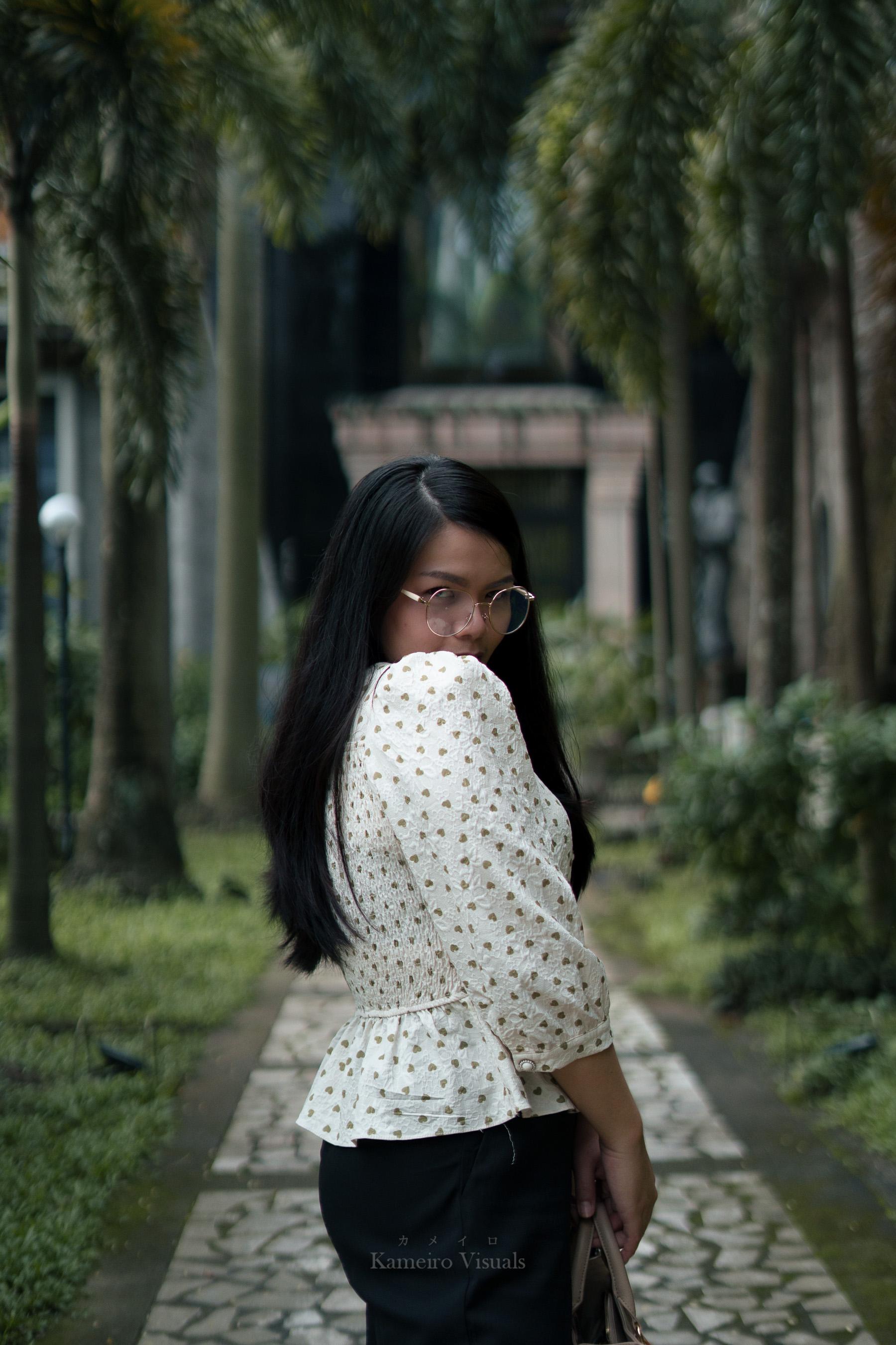 A woman walking outdoors with trees and soft light behind her.