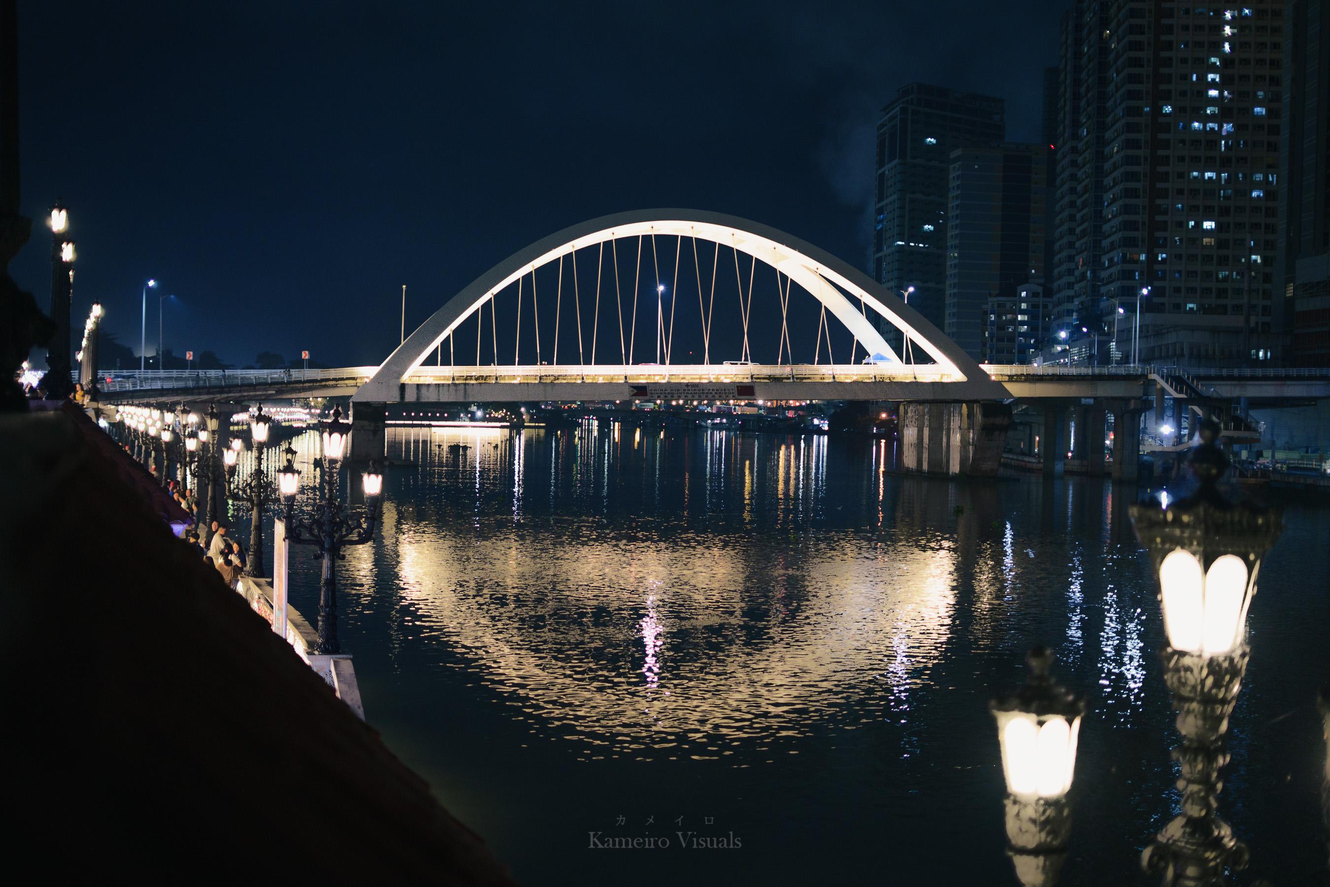 An illuminated arched bridge reflected in the river at night