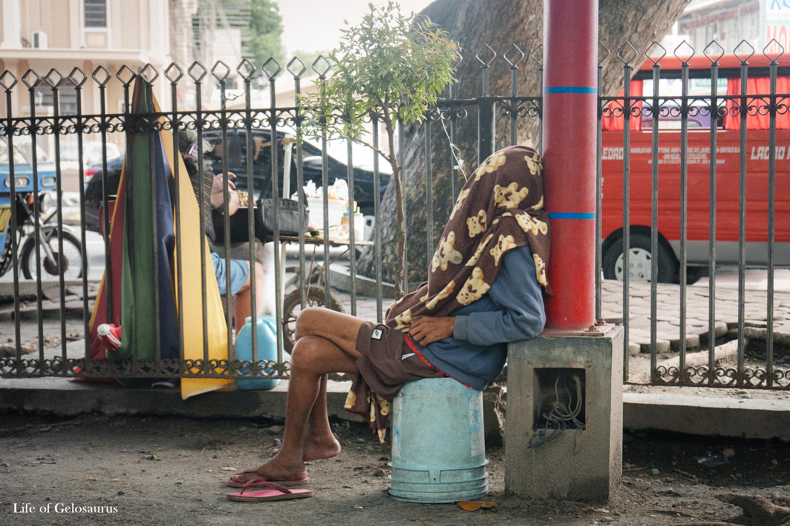 A person seated beside a fence near a red vehicle in General Santos City.