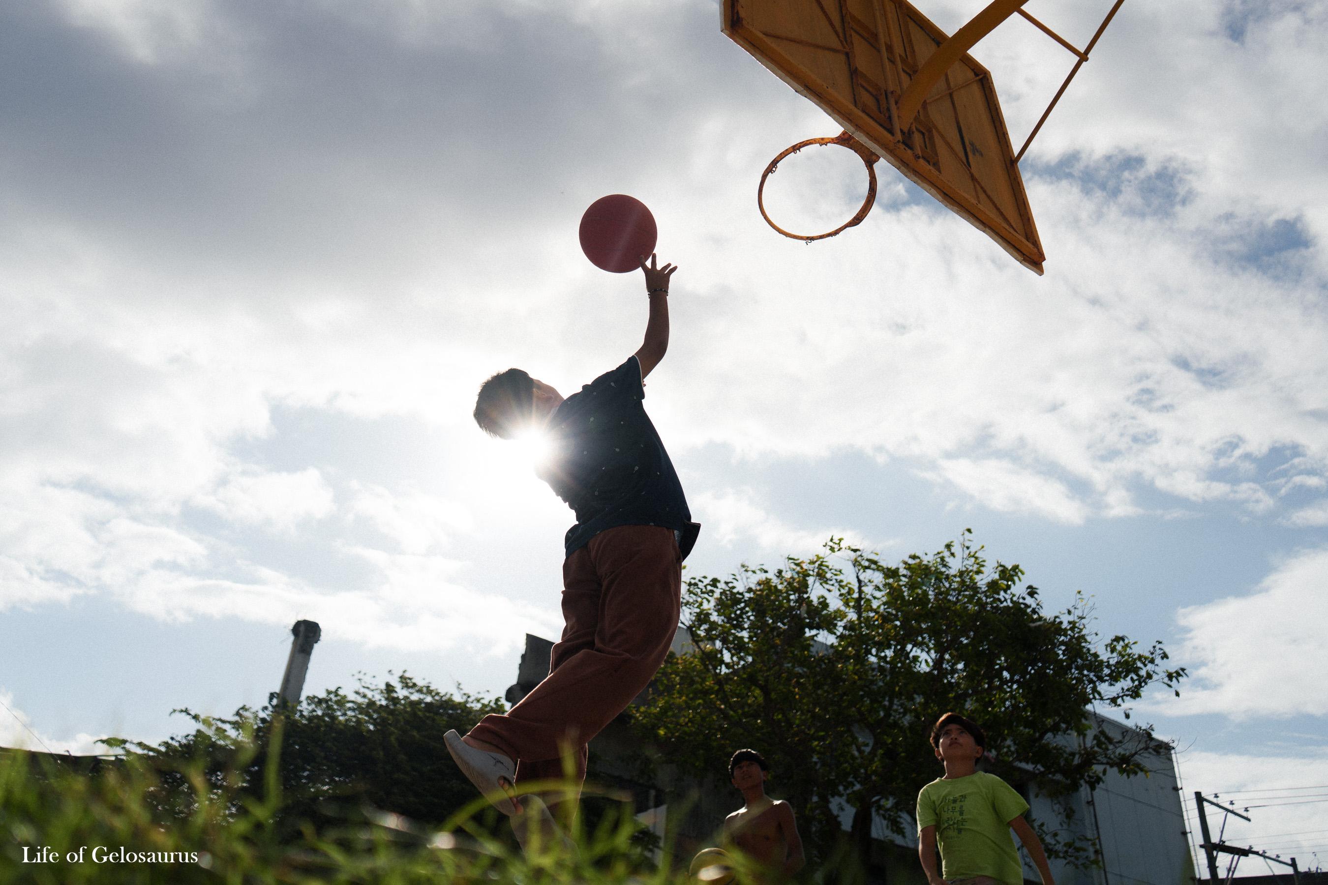 A basketball player reaching toward a hoop beneath a bright sky in General Santos City.